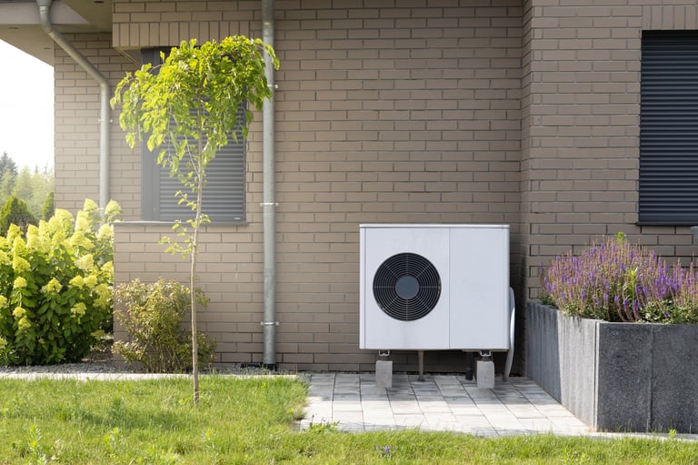 Modern heat pump system installed on the exterior of a building with plants and flowers