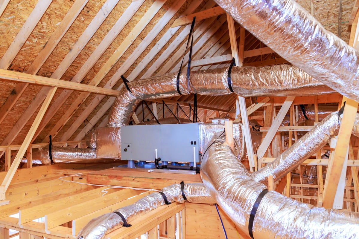 Workers installing ducting ventilation systems in attic of house under construction