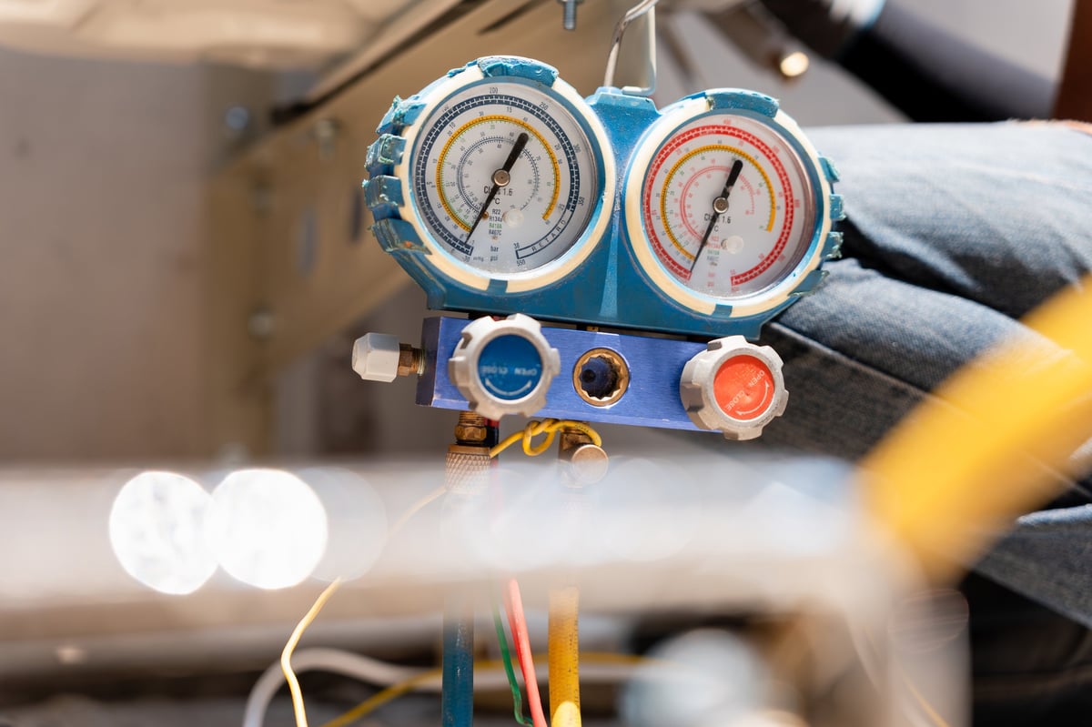 HVAC technician using manifold gauge to measure refrigerant pressure in air conditioning system
