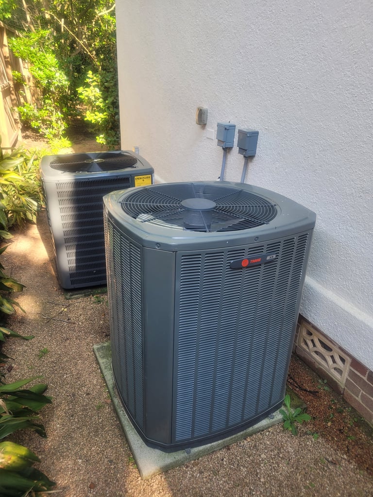 Two outdoor HVAC air conditioning units mounted on concrete pad against white wall with electrical lines